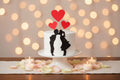 Small white cake with black silhouettes of a couple and red heart-shaped toppers on a white background.